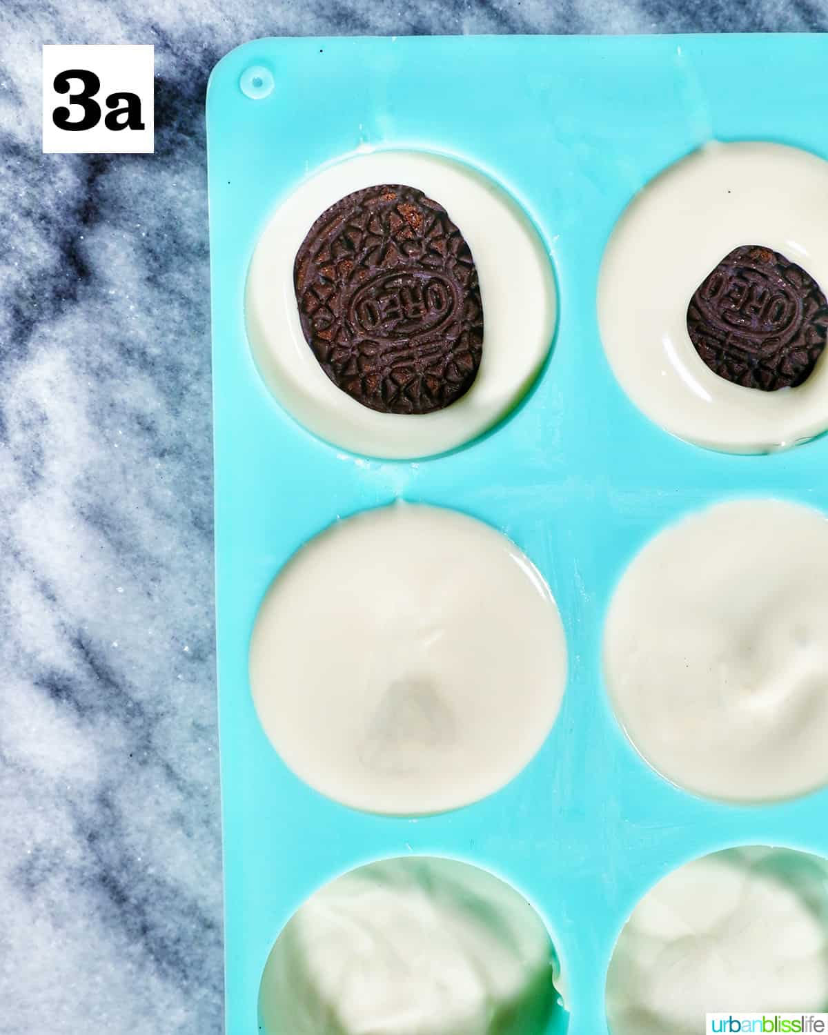 Oreo cookies dunked into melted white chocolate in a blue chocolate candy mold on marble table.