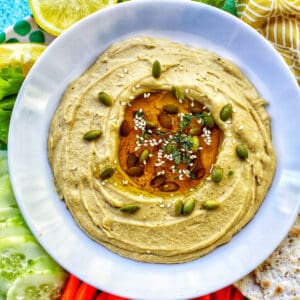 classic hummus in bowl with oil in center and pepitas.