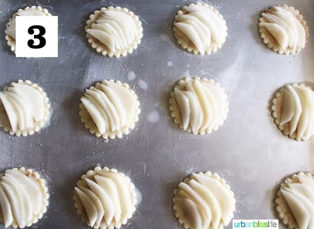 sliced pears in pie dough cups in a baking sheet.