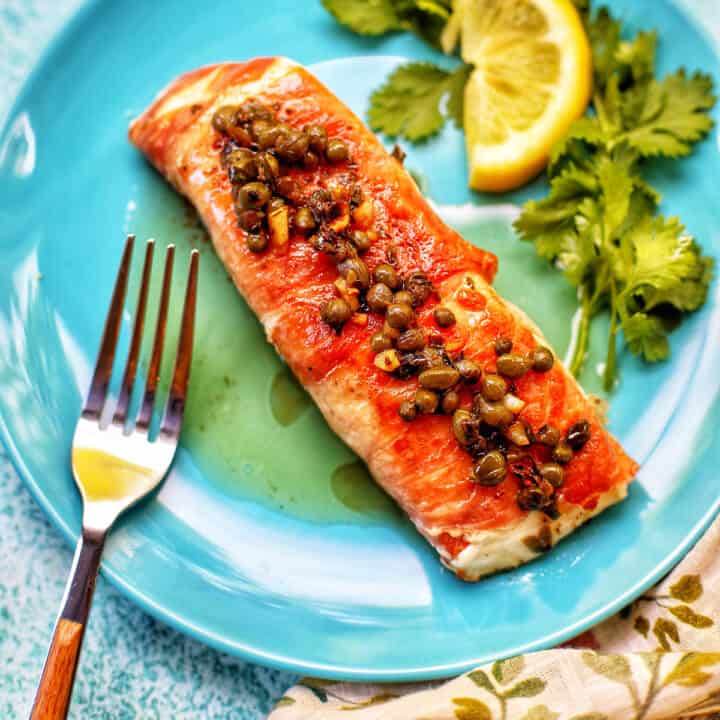 prosciutto wrapped halibut filet with lemon and a fork on a blue plate.