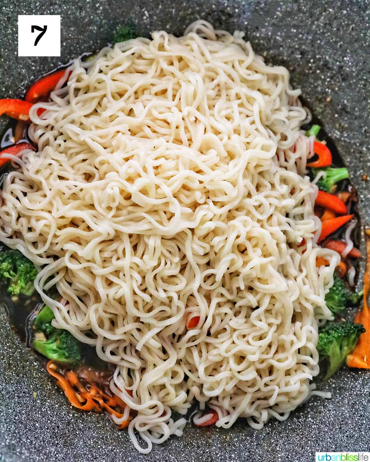 adding noodles to carrots, broccoli, bell peppers in a wok.