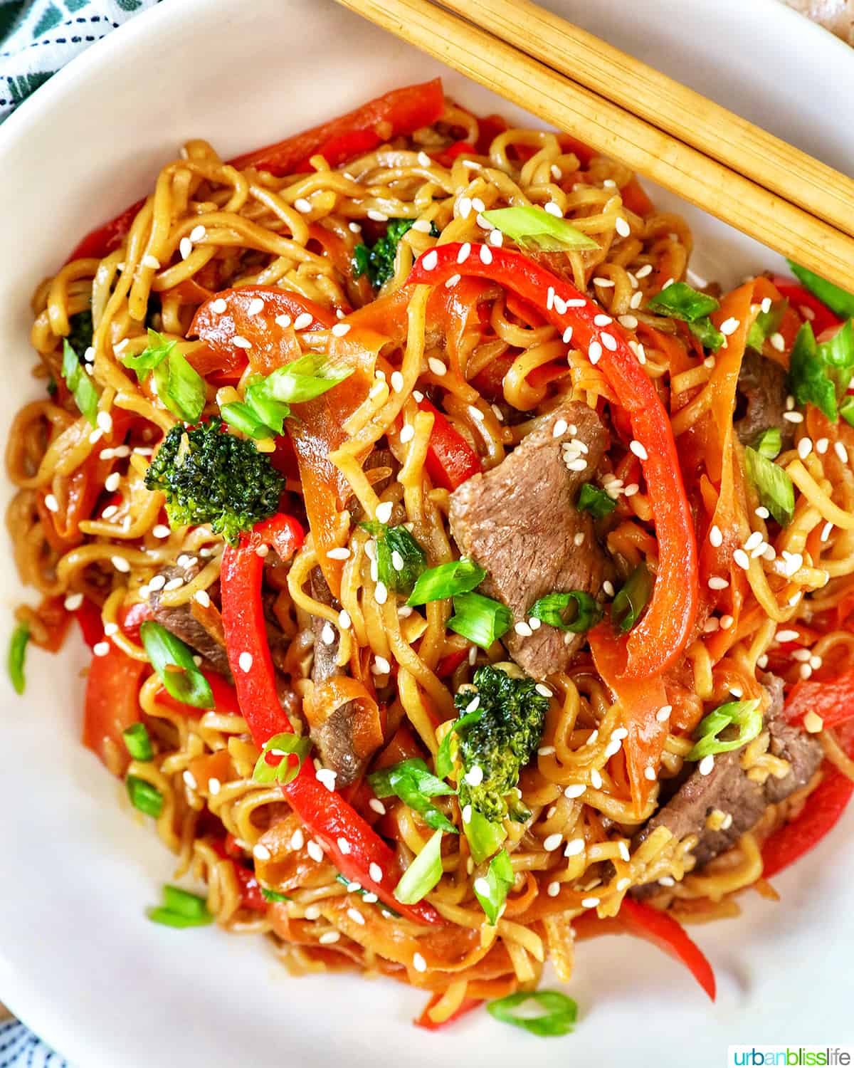 Sesame Garlic Noodles with Steak, broccoli, red peppers, carrots, in a white bowl with chopsticks.