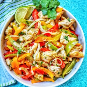 sheet pan chicken fajitas with peppers and a lime in a bowl.