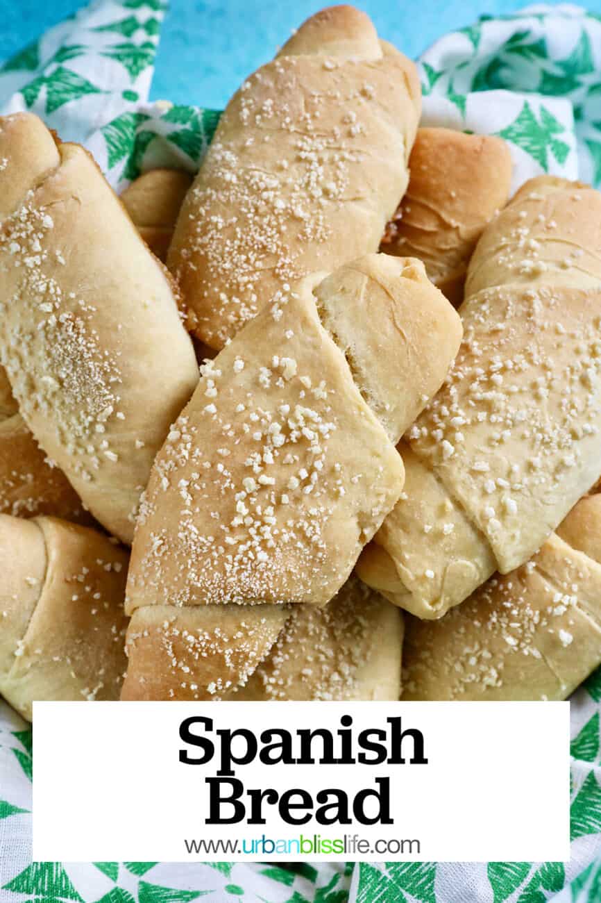 several freshly baked Filipino Spanish bread rolls with breadcrumbs on a green napkin with title text overlay.