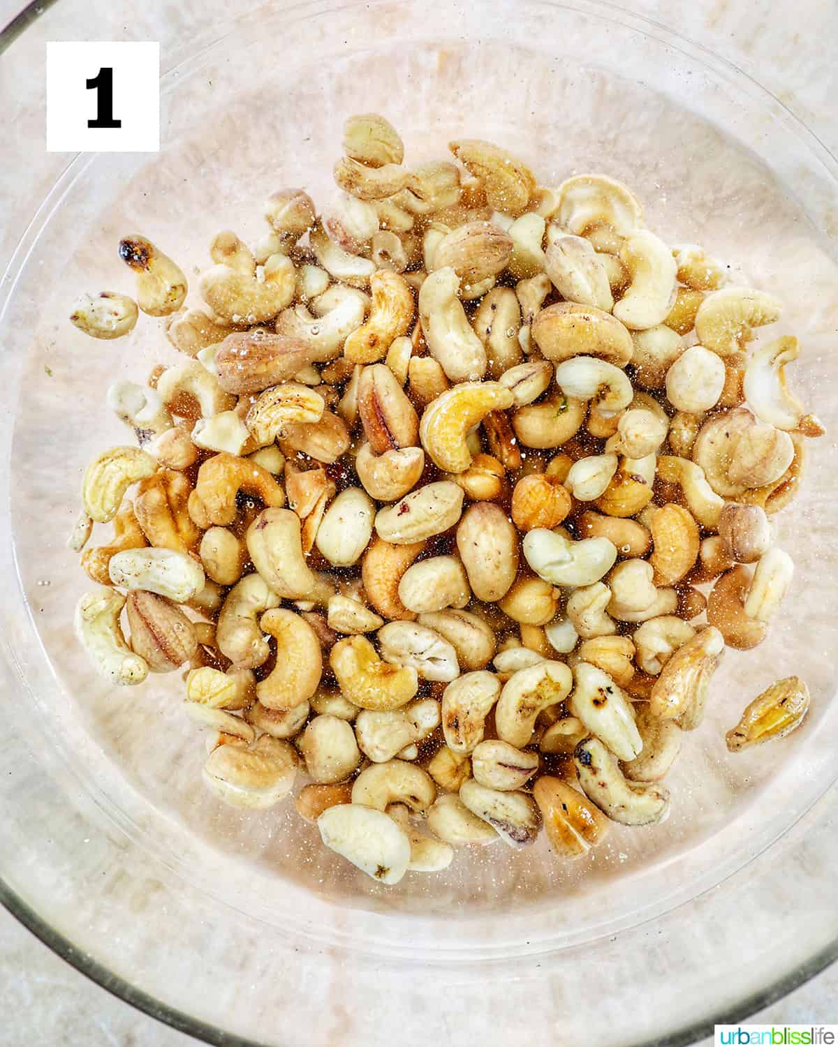 glass bowl of cashews soaking in water on a yellow table.