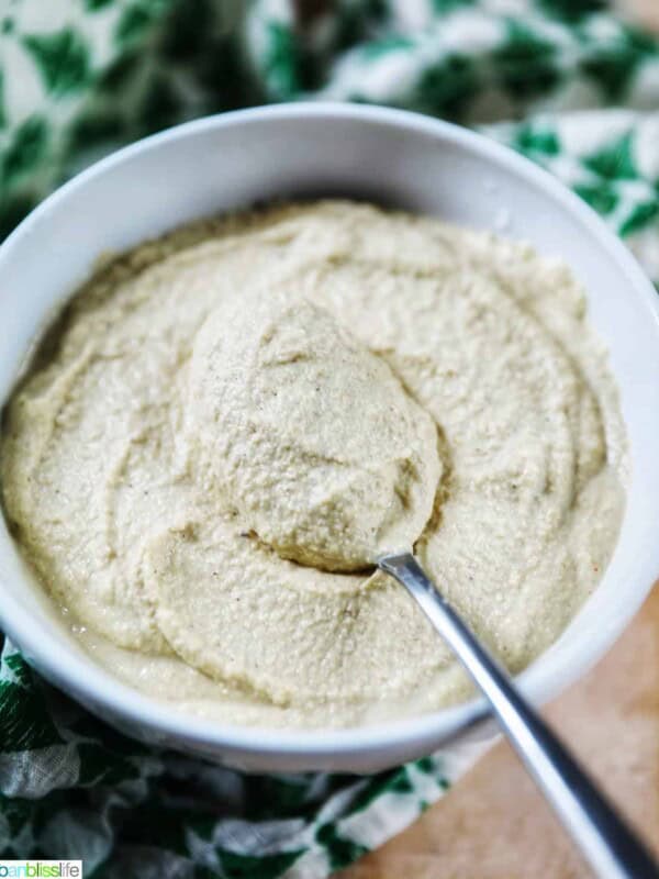 whitwhite bowl of Vegan Cashew Cheese with spoon in bowl, with green and white napkin underneath.