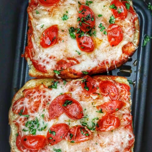 two half loaves of french bread pizza in an air fryer basket.