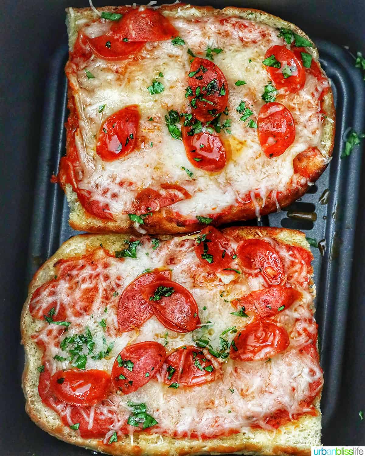 two half loaves of french bread pizza in an air fryer basket.