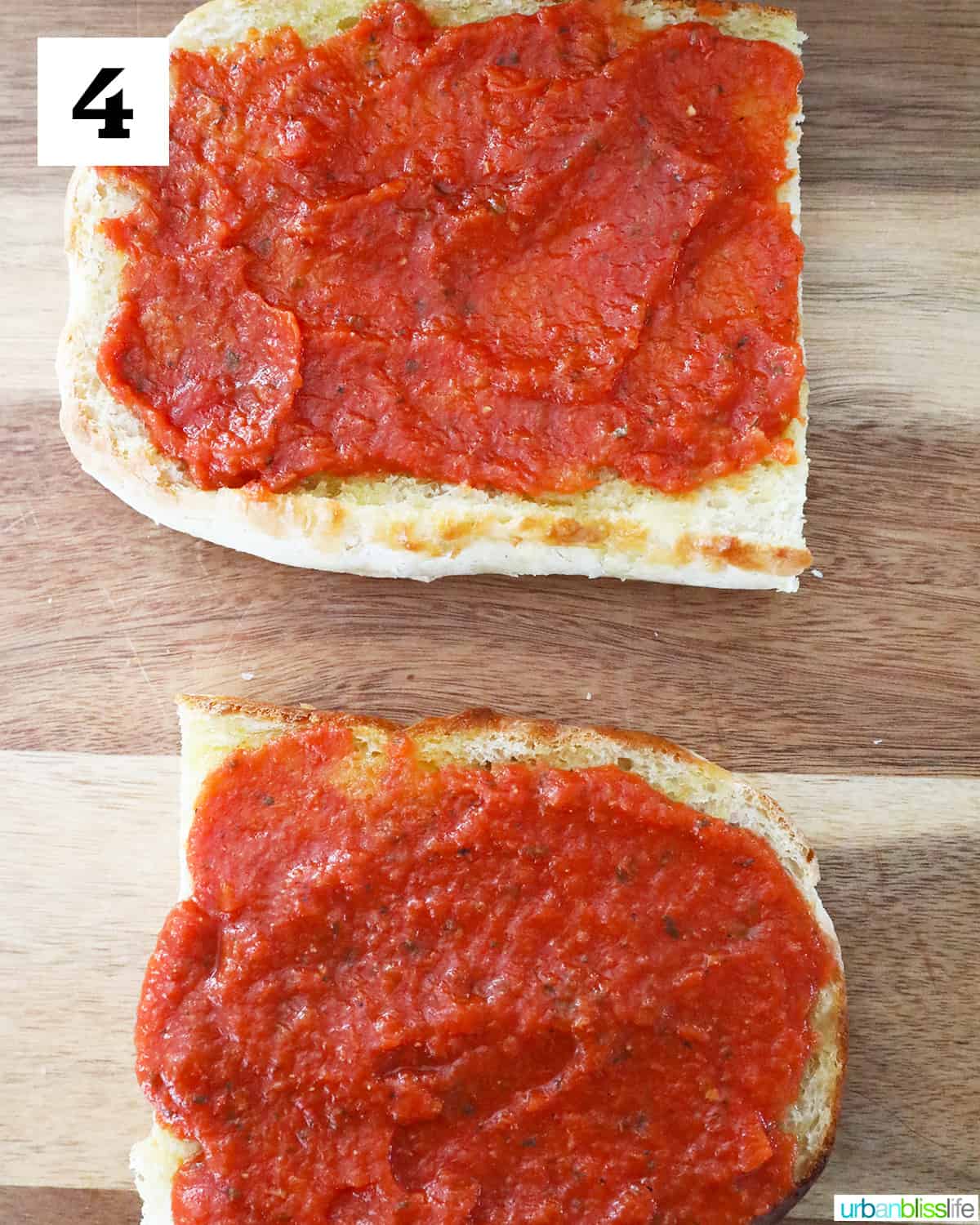 two halves of french bread topped with pizza sauce on a cutting board.