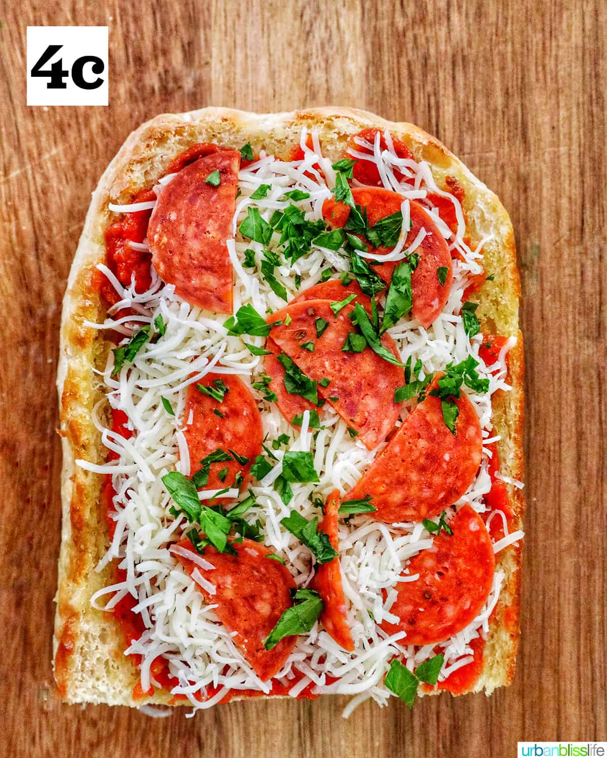 two halves of french bread topped with pizza sauce, cheese and parsley on a cutting board.