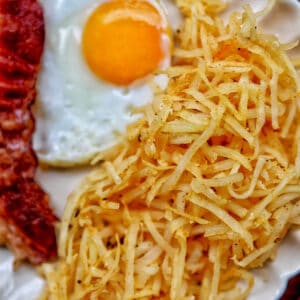 air fryer hash browns with a fried egg and bacon.