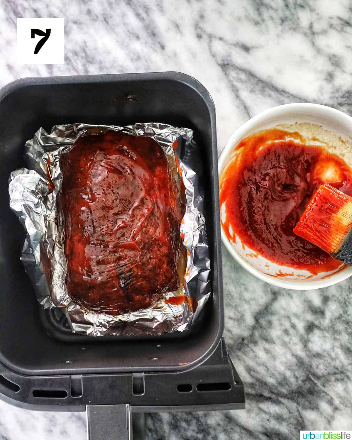 meatloaf in foil in an air fryer basket with sauce on the side.