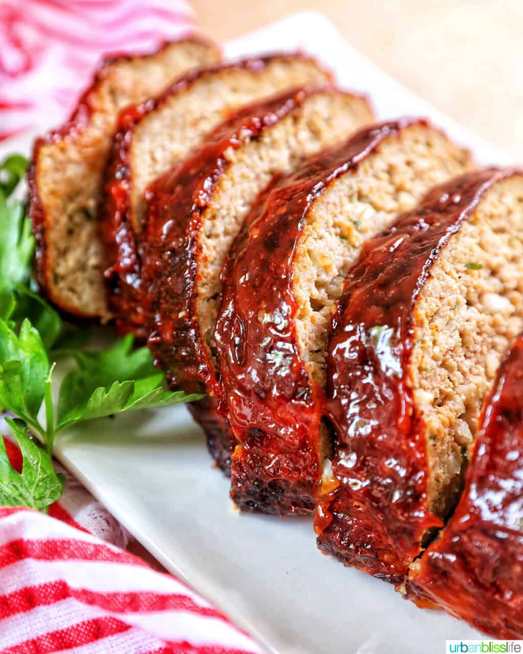 glazed slices of air fryer meatloaf on a white plate with greens and red striped napkin..