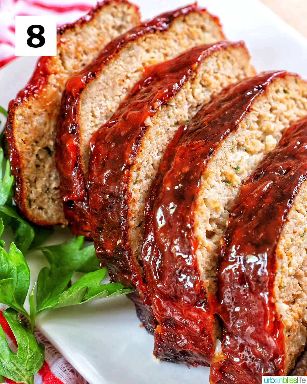 glazed slices of air fryer meatloaf on a white plate with greens and red striped napkin..