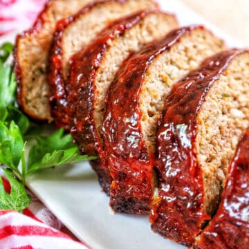 glazed slices of air fryer meatloaf on a white plate with greens and red striped napkin..