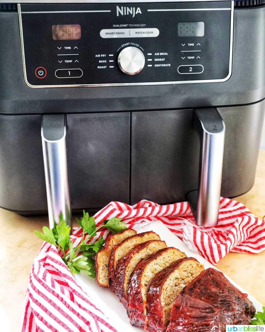 Ninja Foodi air fryer behind a plate of sliced meatloaf with red striped napkin.