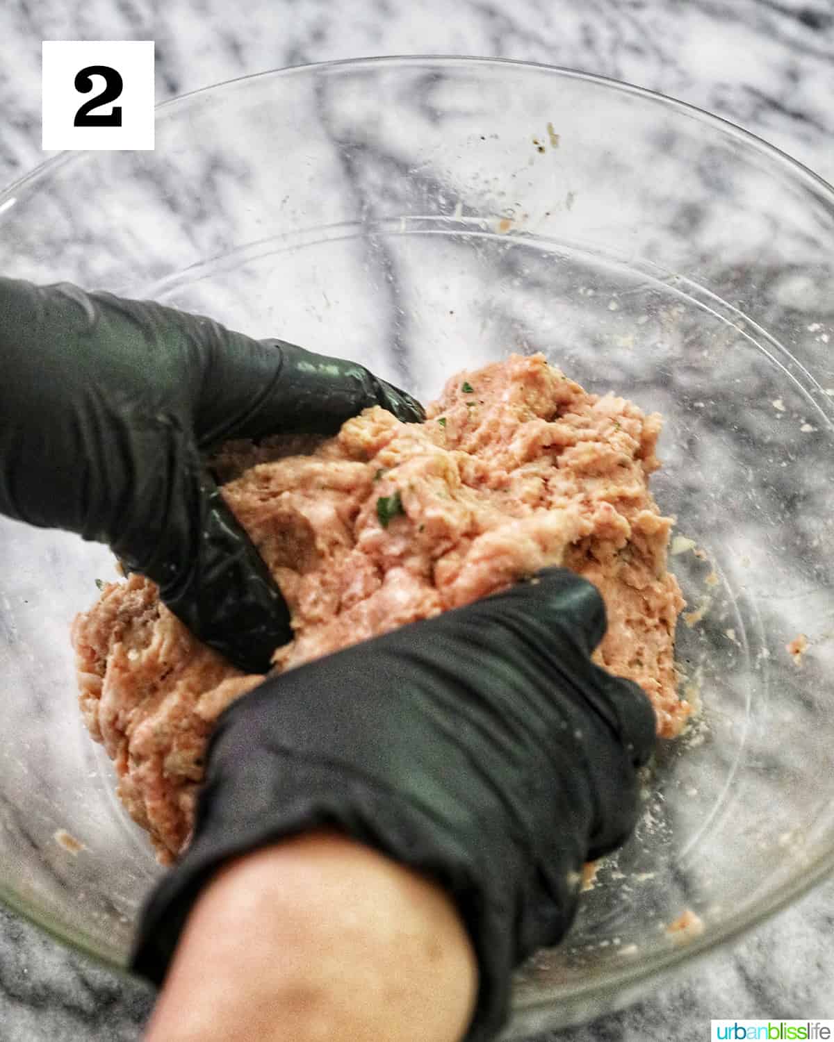 hands in black gloves forming a meatloaf with the ingredients in a glass bowl on top of marble table.