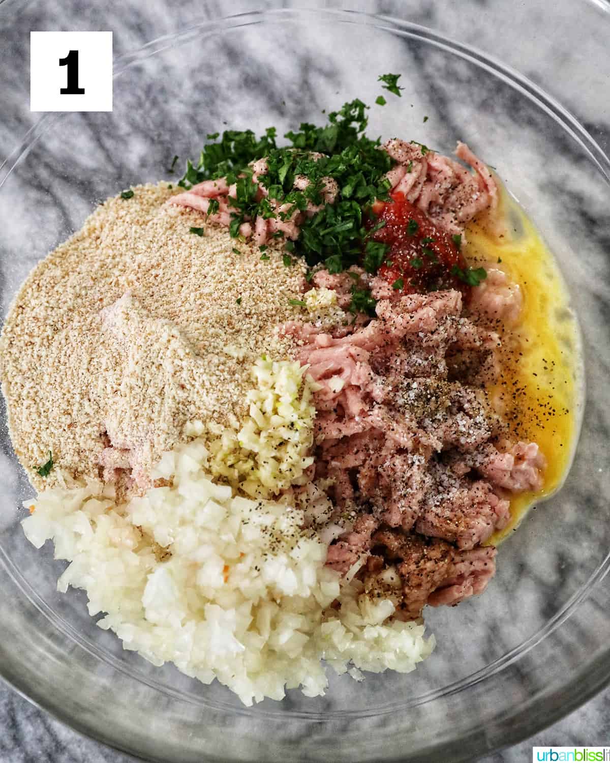 ingredients to make meatloaf in a clear glass bowl on top of marble.