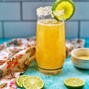 champagne margarita in a tall glass with lime slices.