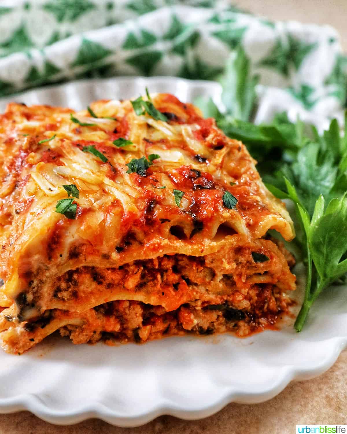 side view of multi-layered dairy free lasagna on a white plate with green and white napkin in background.