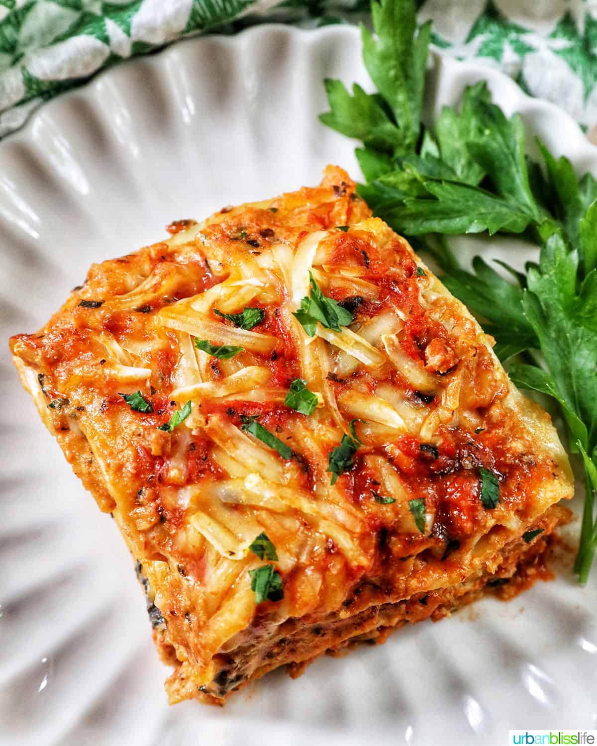 top view of multi-layered dairy free lasagna on a white plate with parsley on the side.