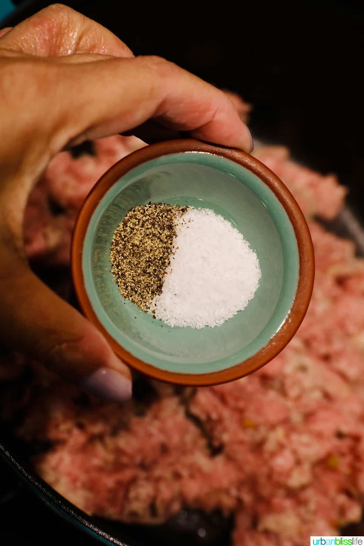 hand holding a pinch bowl of salt and pepper to add to the pot.