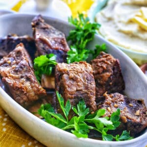 filipino short ribs adobo in a serving dish with herbs.