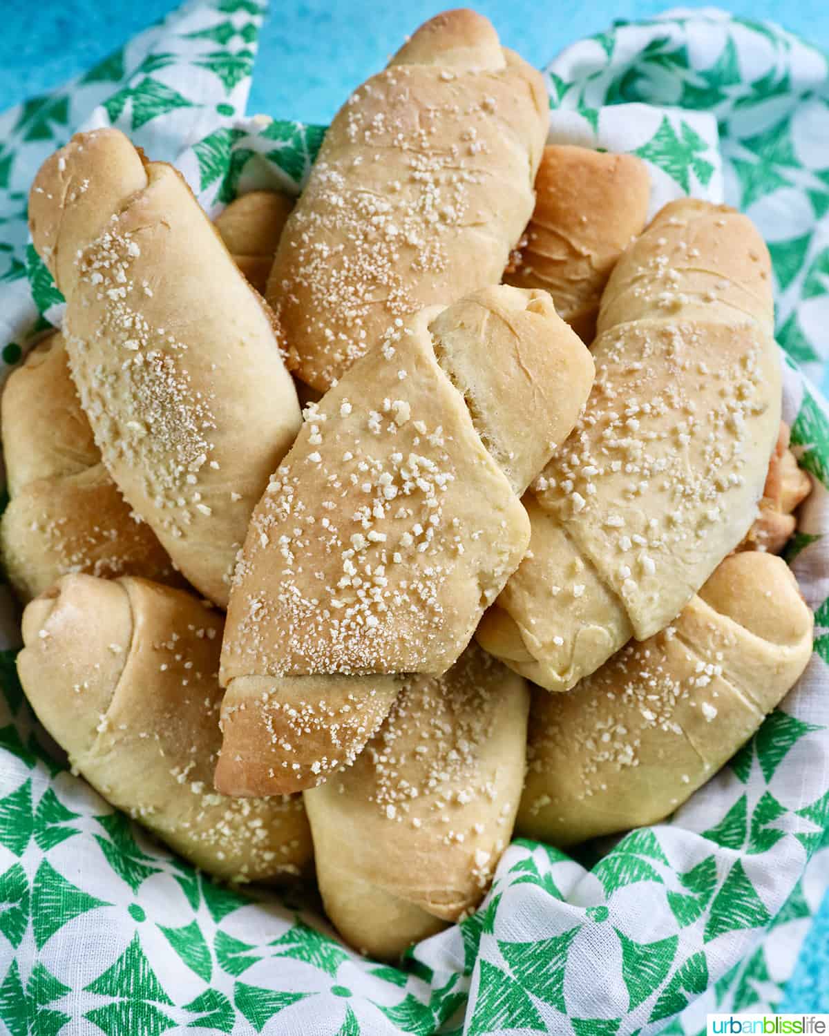 several freshly baked Filipino Spanish bread rolls with breadcrumbs on a green and white napkin.