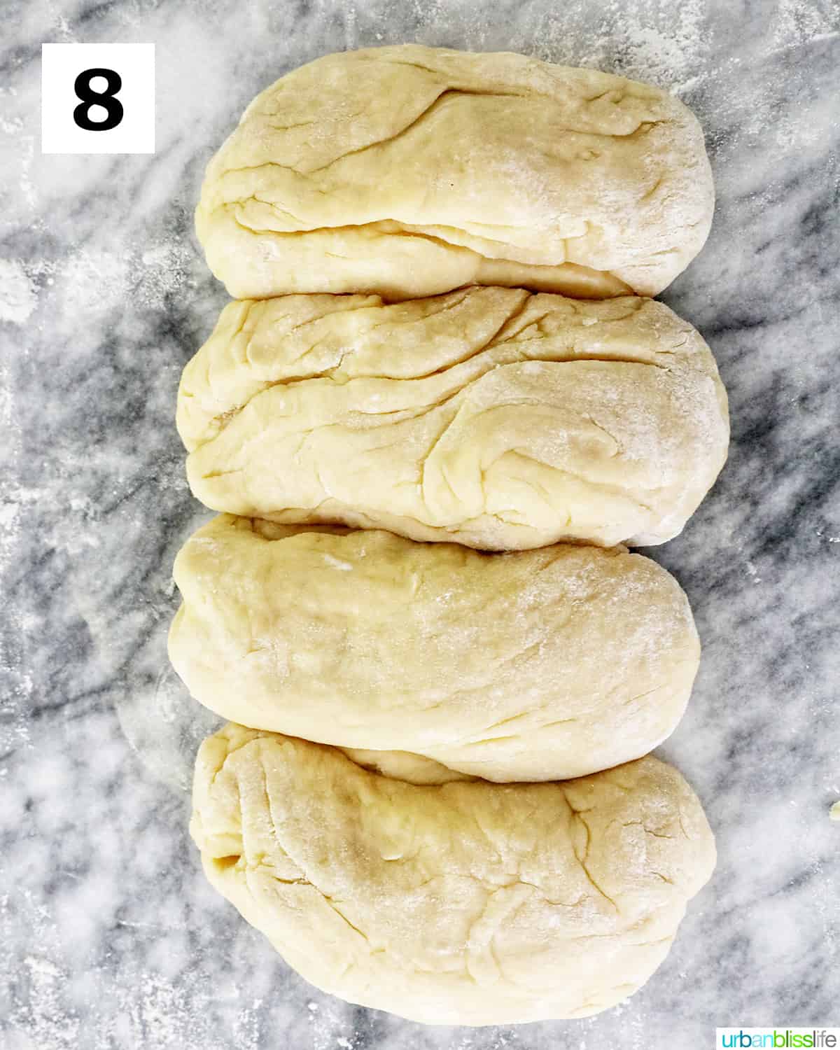 four pieces of dough divided out to make Spanish bread, on a marble counter.