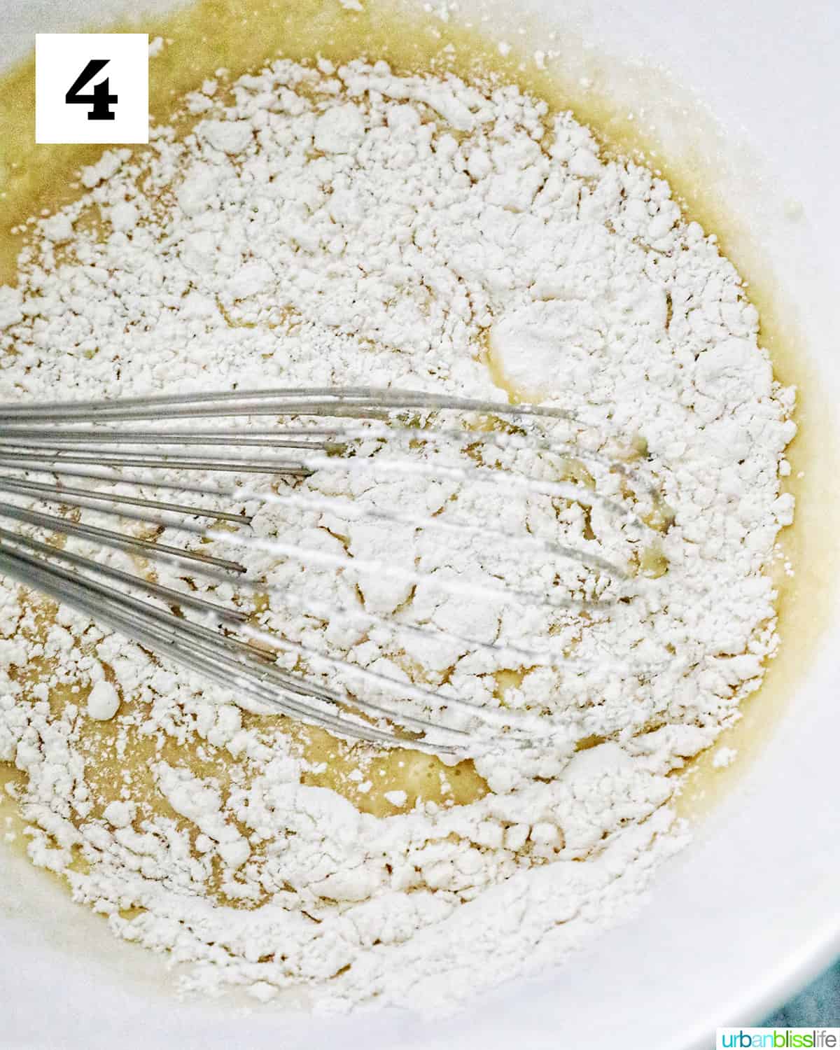 whisking in flour into wet ingredients in a white bowl to make spanish bread.