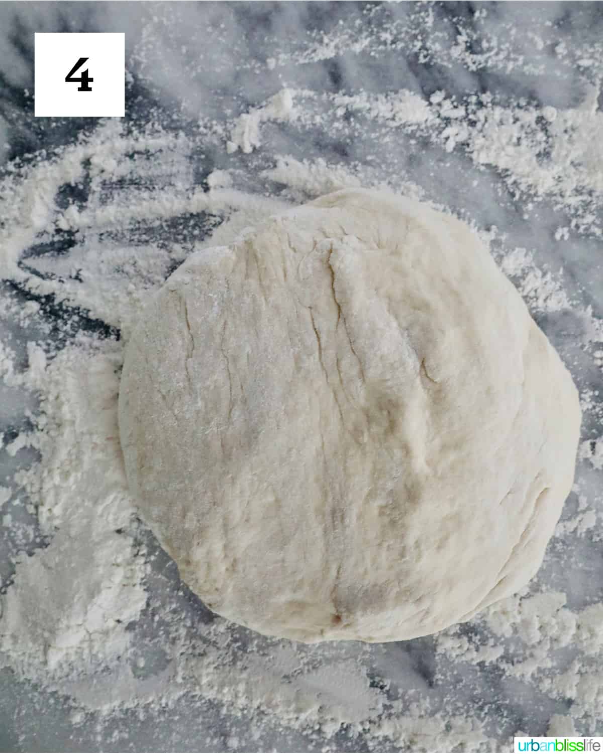 homemade French bread dough ball on a floured marble countertop.