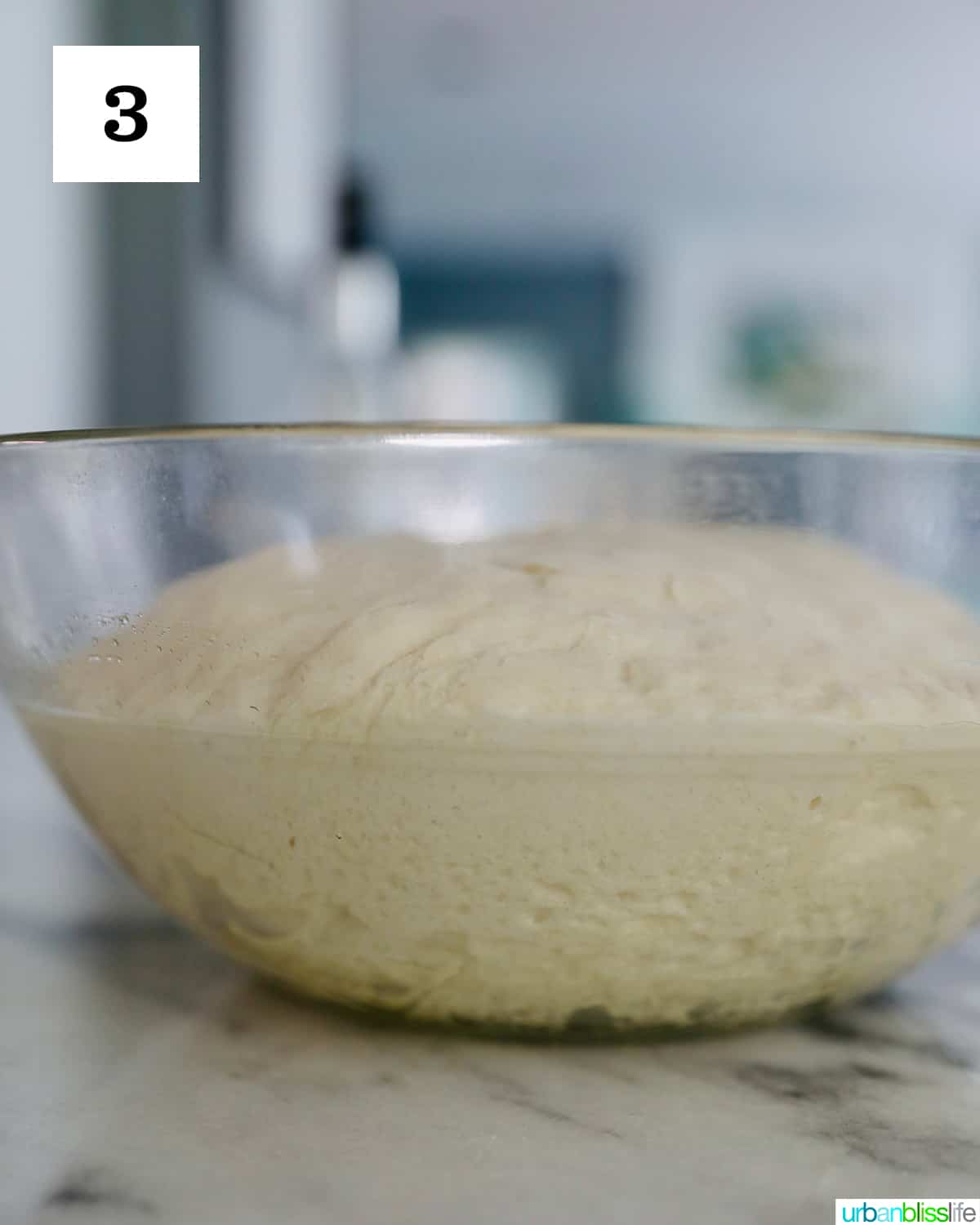 french bread dough risen to twice its starting size in a glass bowl.
