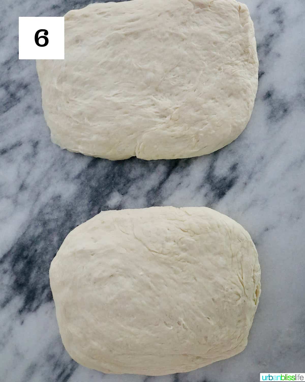 Two homemade French bread dough balls on a floured marble countertop.
