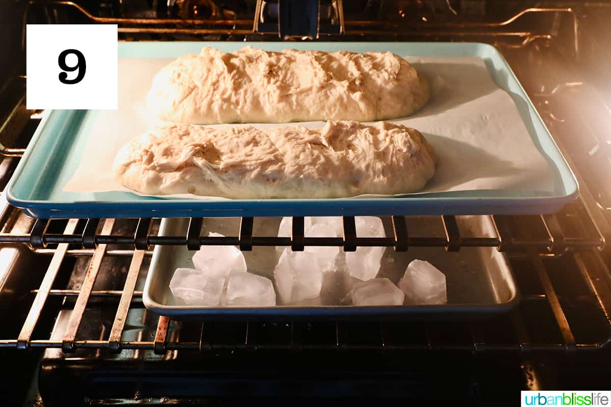 two french bread loaves baking in an oven with a sheet of ice beneath it.