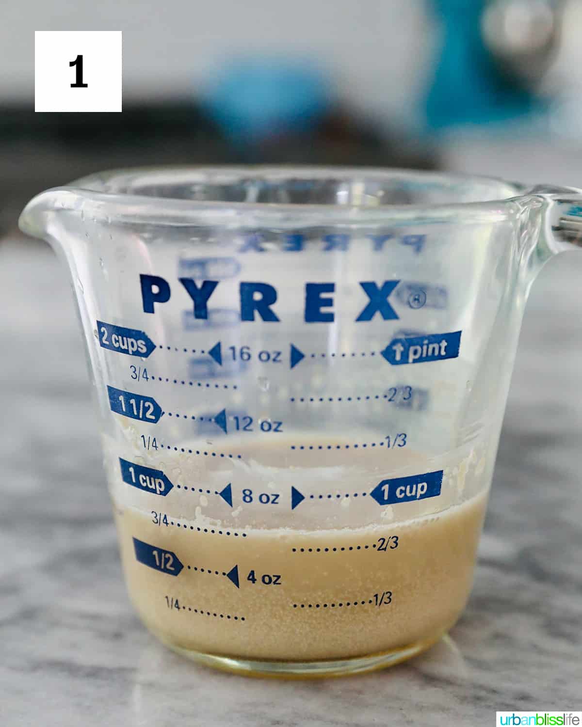 glass Pyrex measuring cup with yeast rising on a marble countertop.