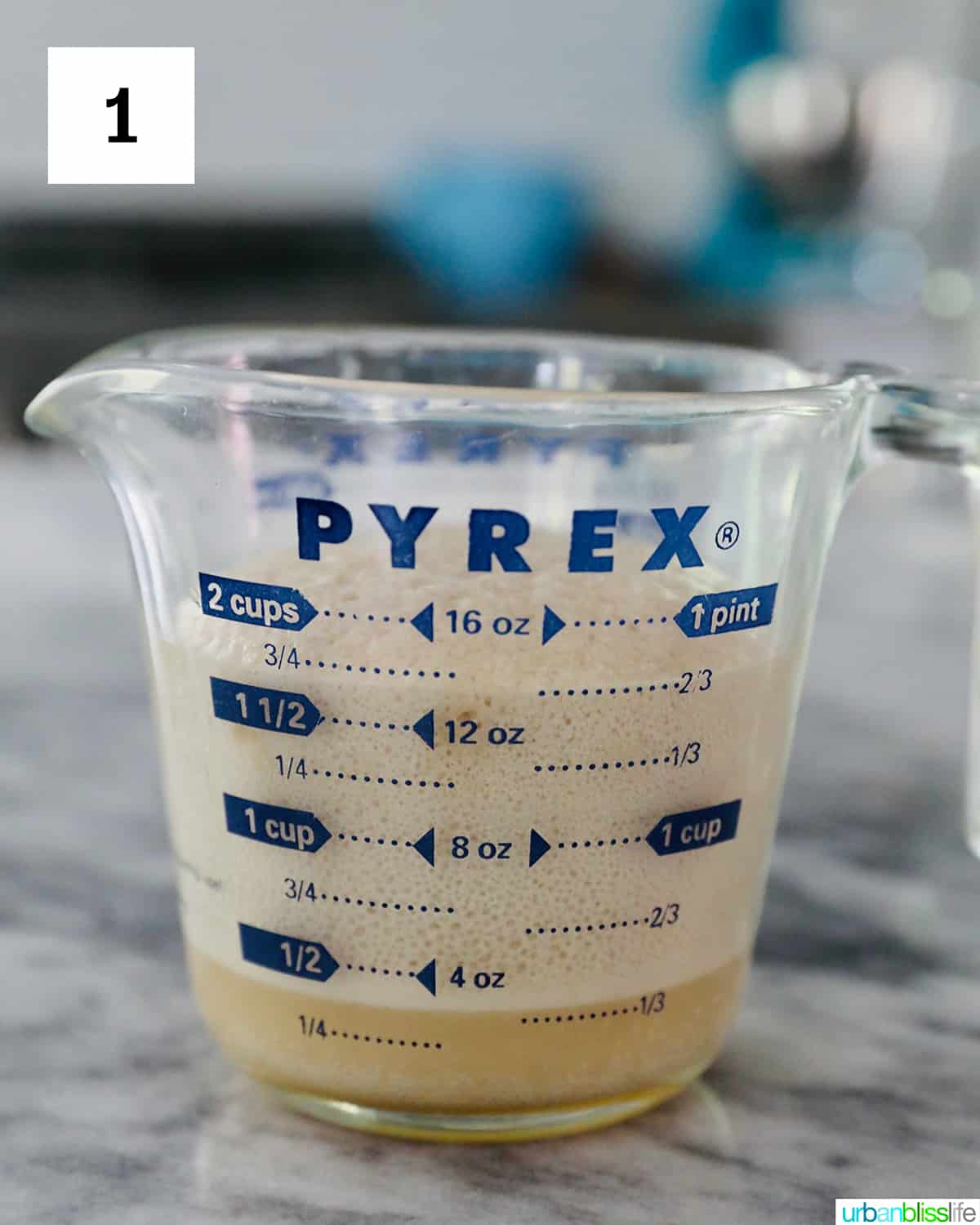 glass Pyrex measuring cup with yeast rising on a marble countertop.
