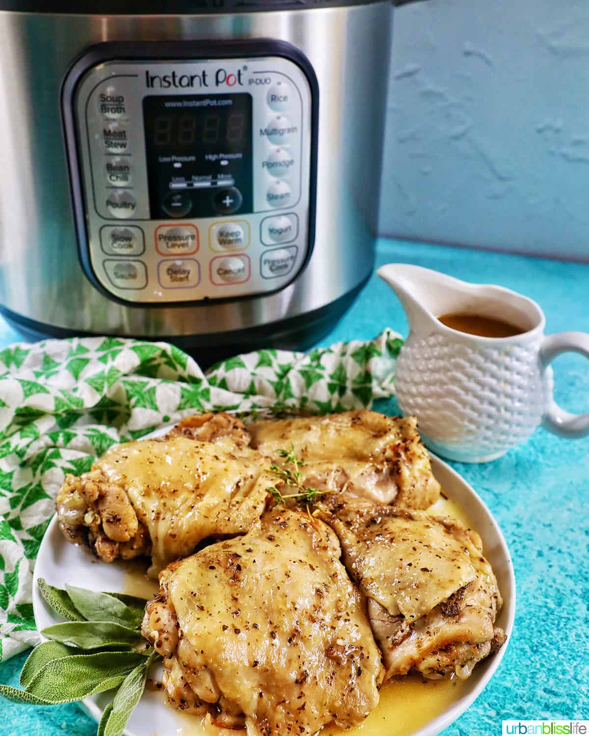 Instant pot electric pressure cooker behind a plate full of cooked chicken thighs and a pitcher of gravy on a blue background.