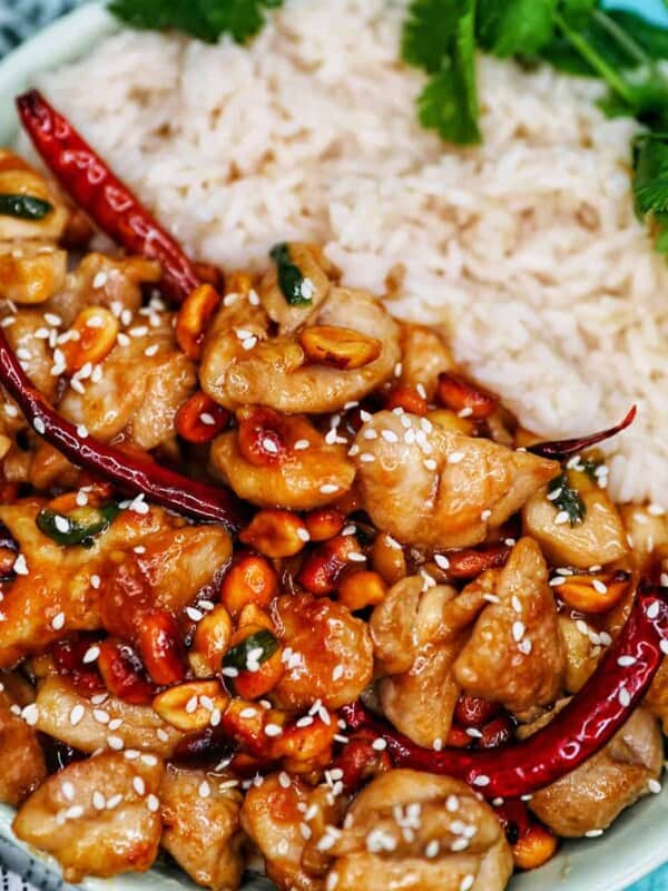chopped chicken pieces in a kung pao sauce on rice in a white bowl with greens.