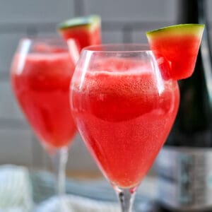 two glasses of watermelon mimosas with slice of watermelon garnish.