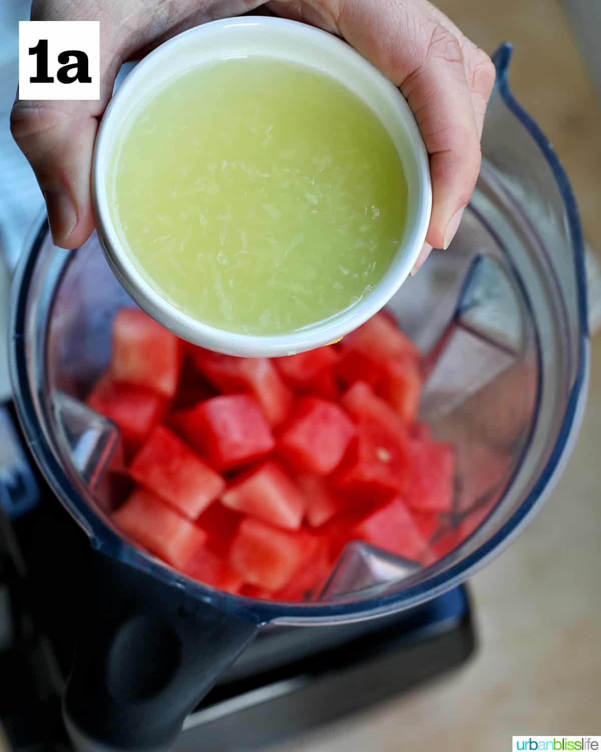 hand adding lime juice in a small bowl into a blender with cubed watermelons.