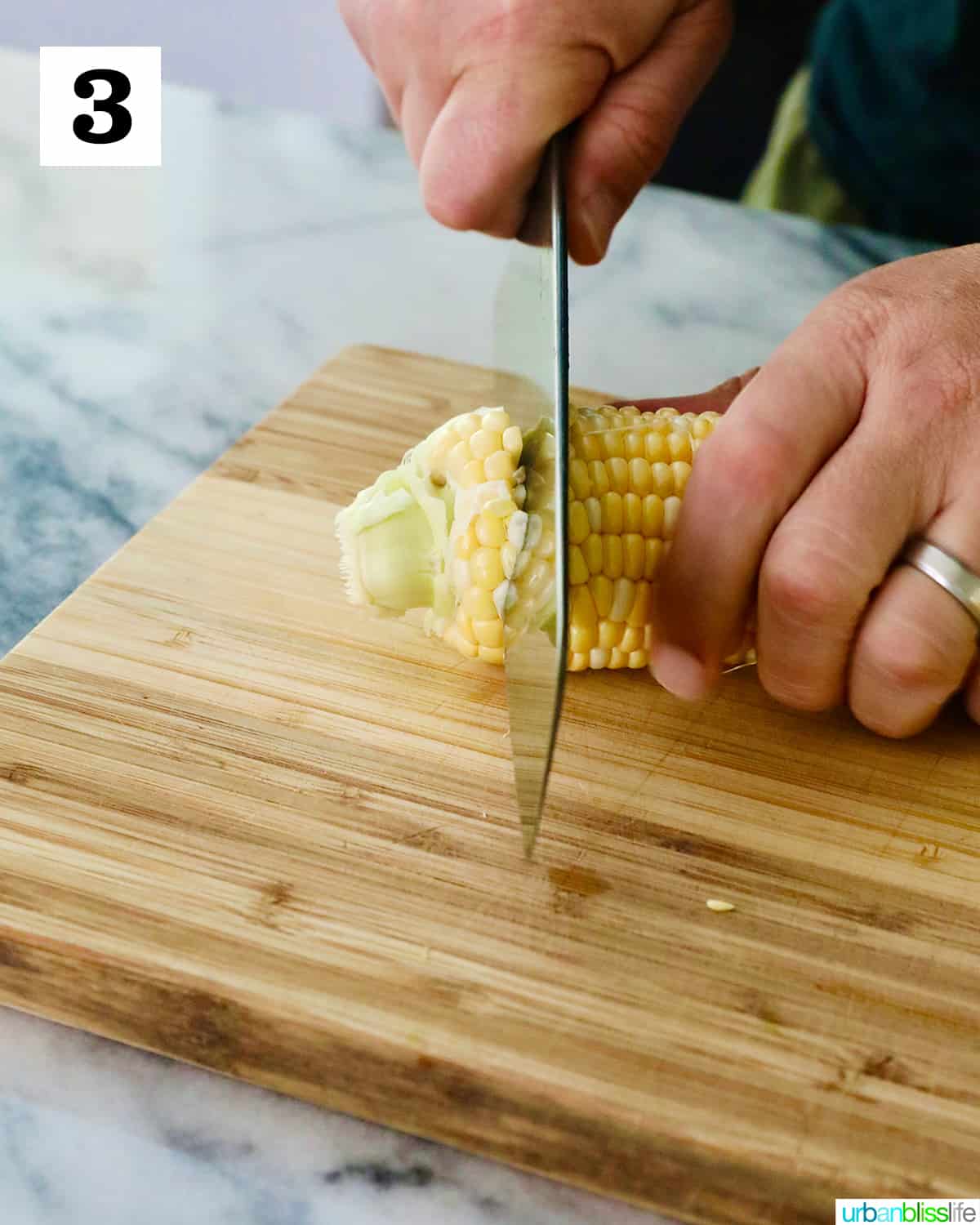 hands using a knife to slice off the end of a corn cob on a cutting board.