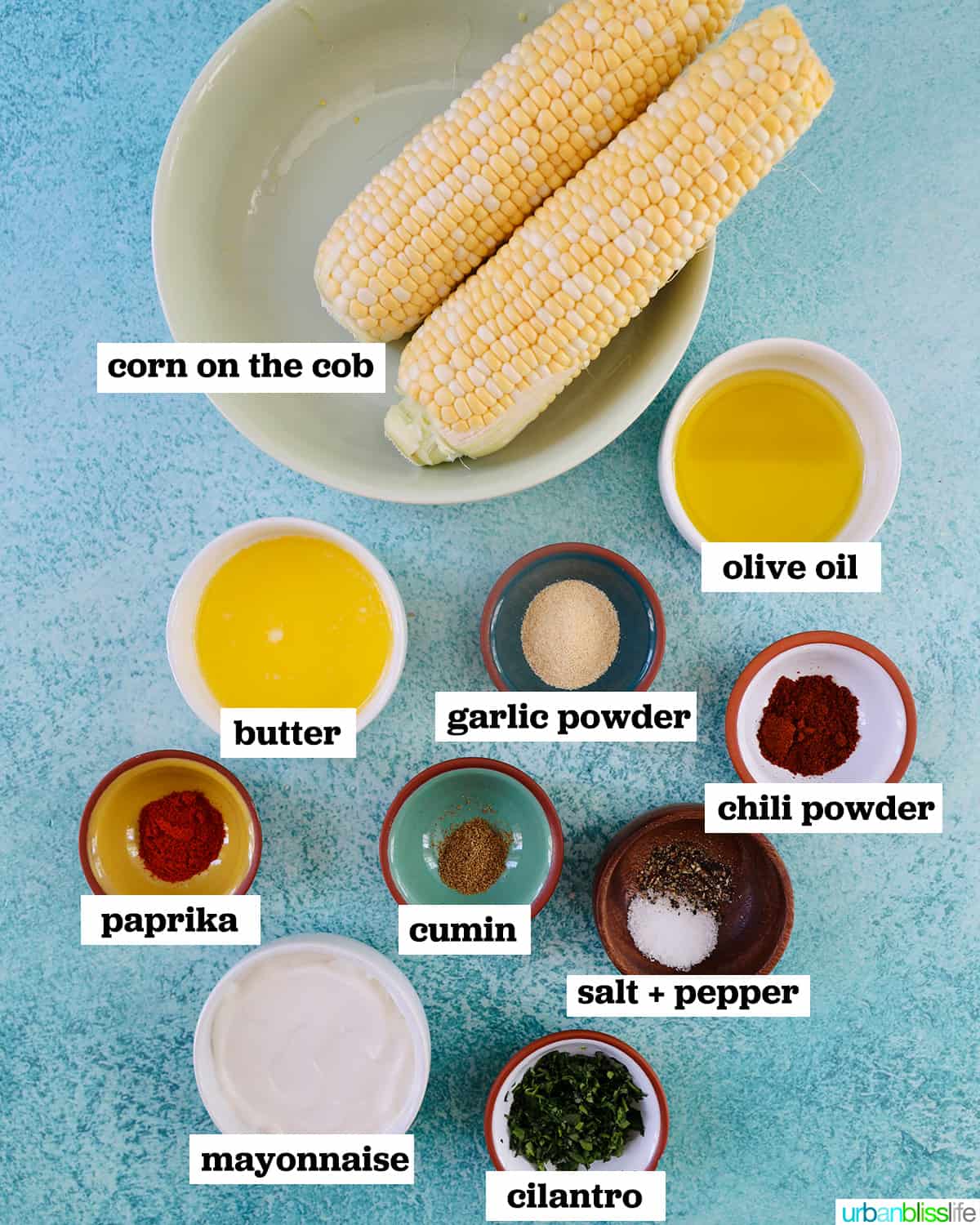 ingredients in bowls to make air fryer corn ribs, on a blue table, with labeled ingredients..