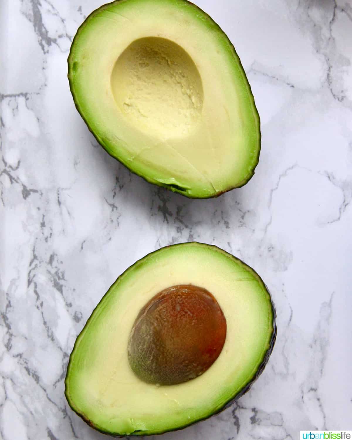 Avocado split in half with flesh and pit facing up, on a marble countertop.