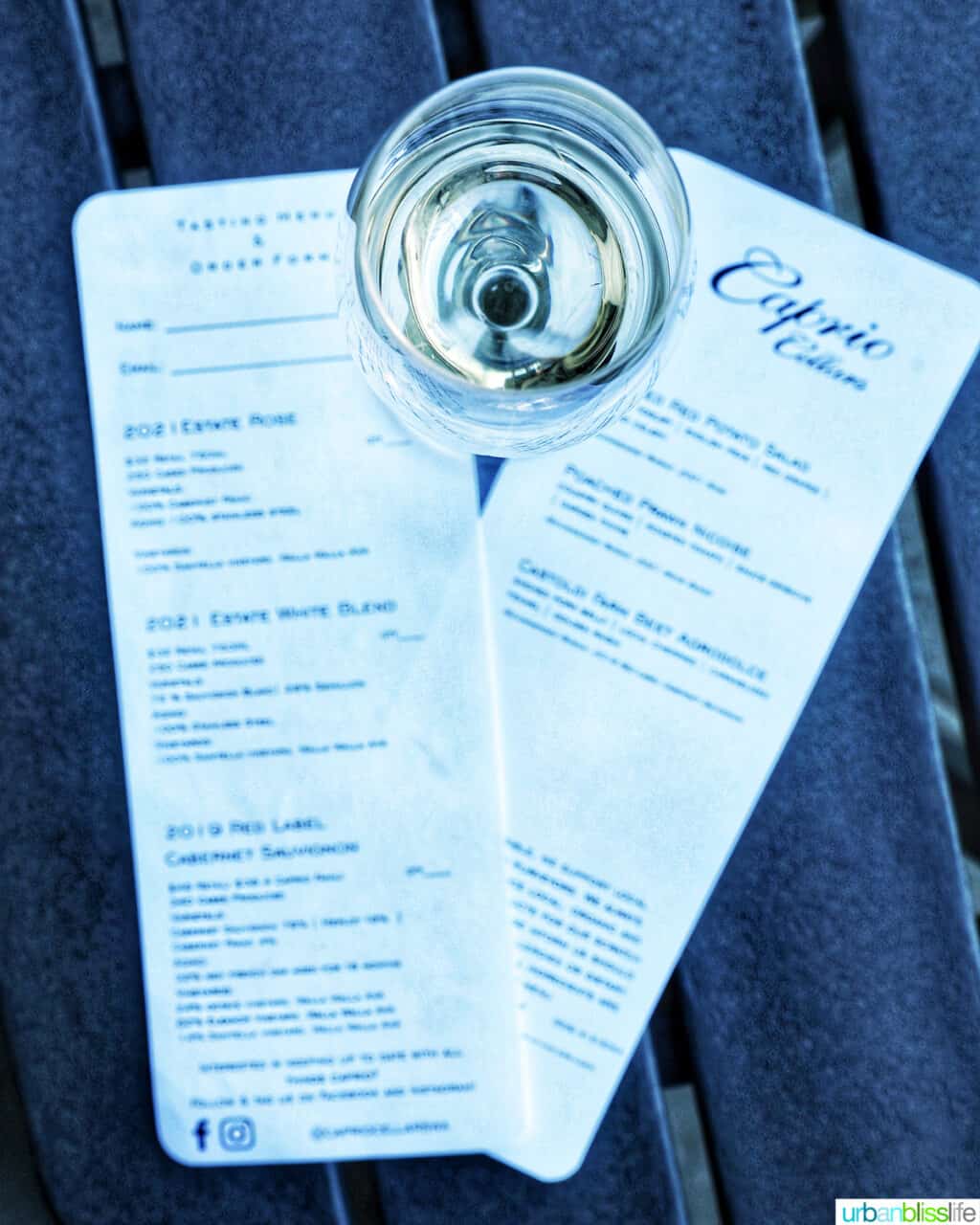 glass of sparkling wine on top of Caprio Cellars food and wine menus on a black table.