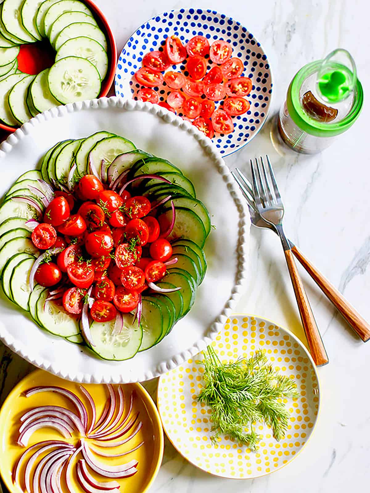 Cucumber tomato salad overhead with two forks and a bottle of dressing.