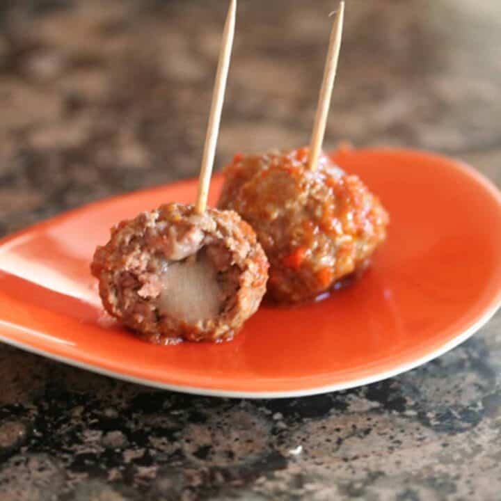 two manchego-stuffed meatballs on an orange plate with toothpicks.