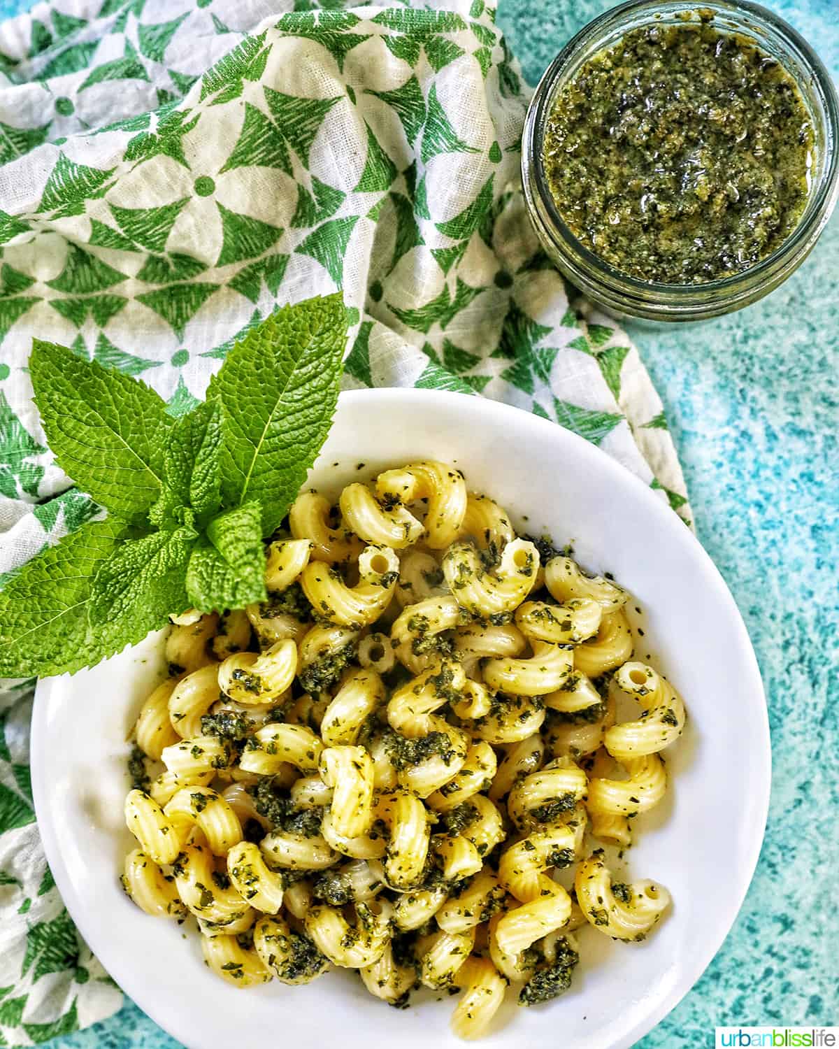 pesto pasta in a white bowl on blue background with a side of pesto pasta in a jar.
