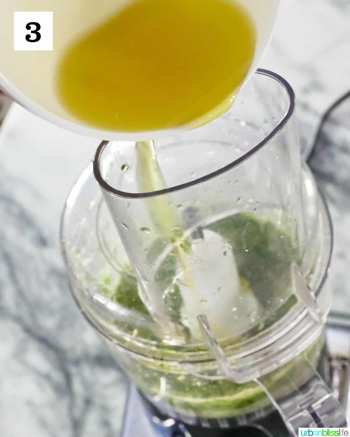 white bowl with olive oil pouring into a food processor making mint pesto.