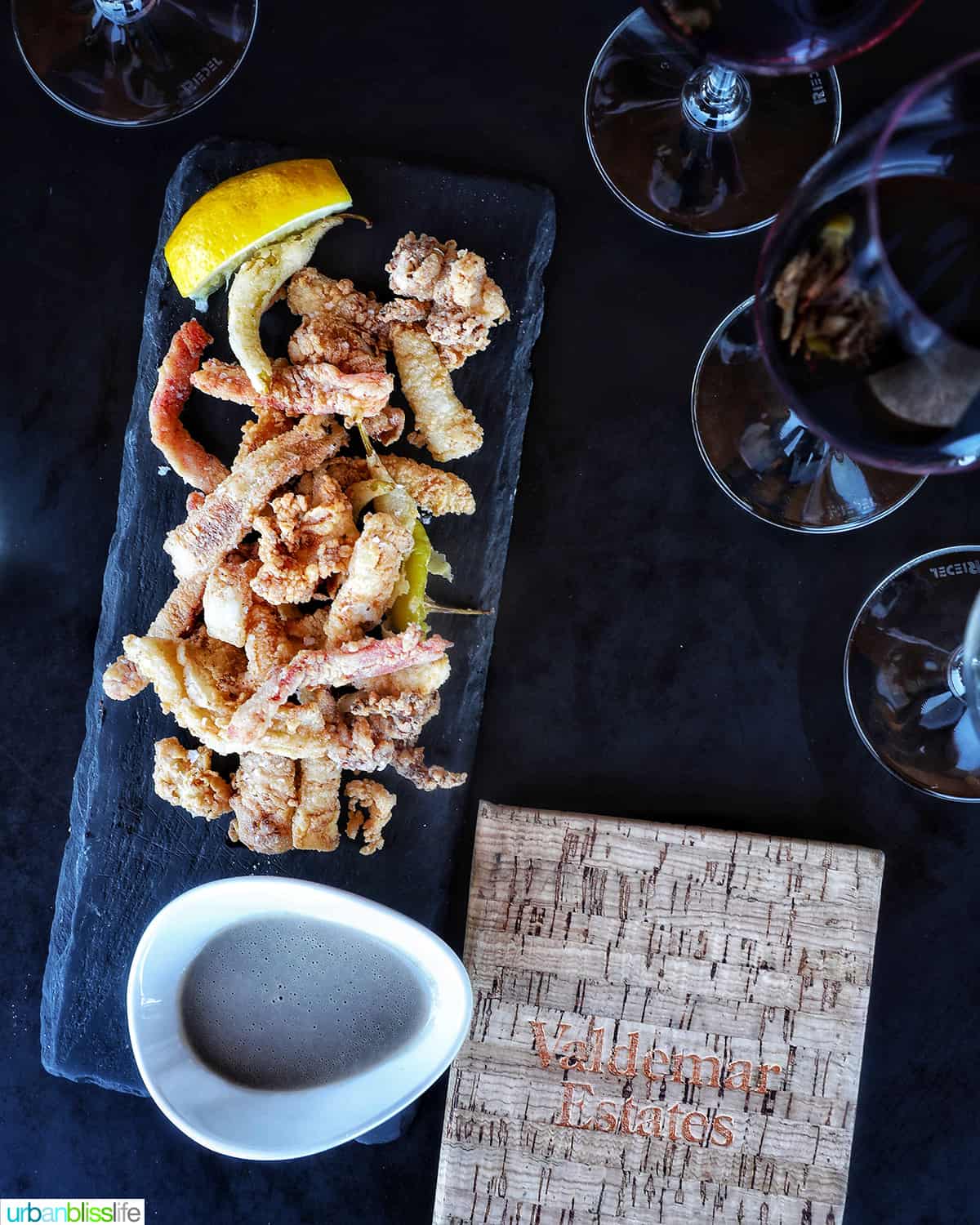 black stone serving plate of fried calamari next to a tasting menu and glasses of wine.