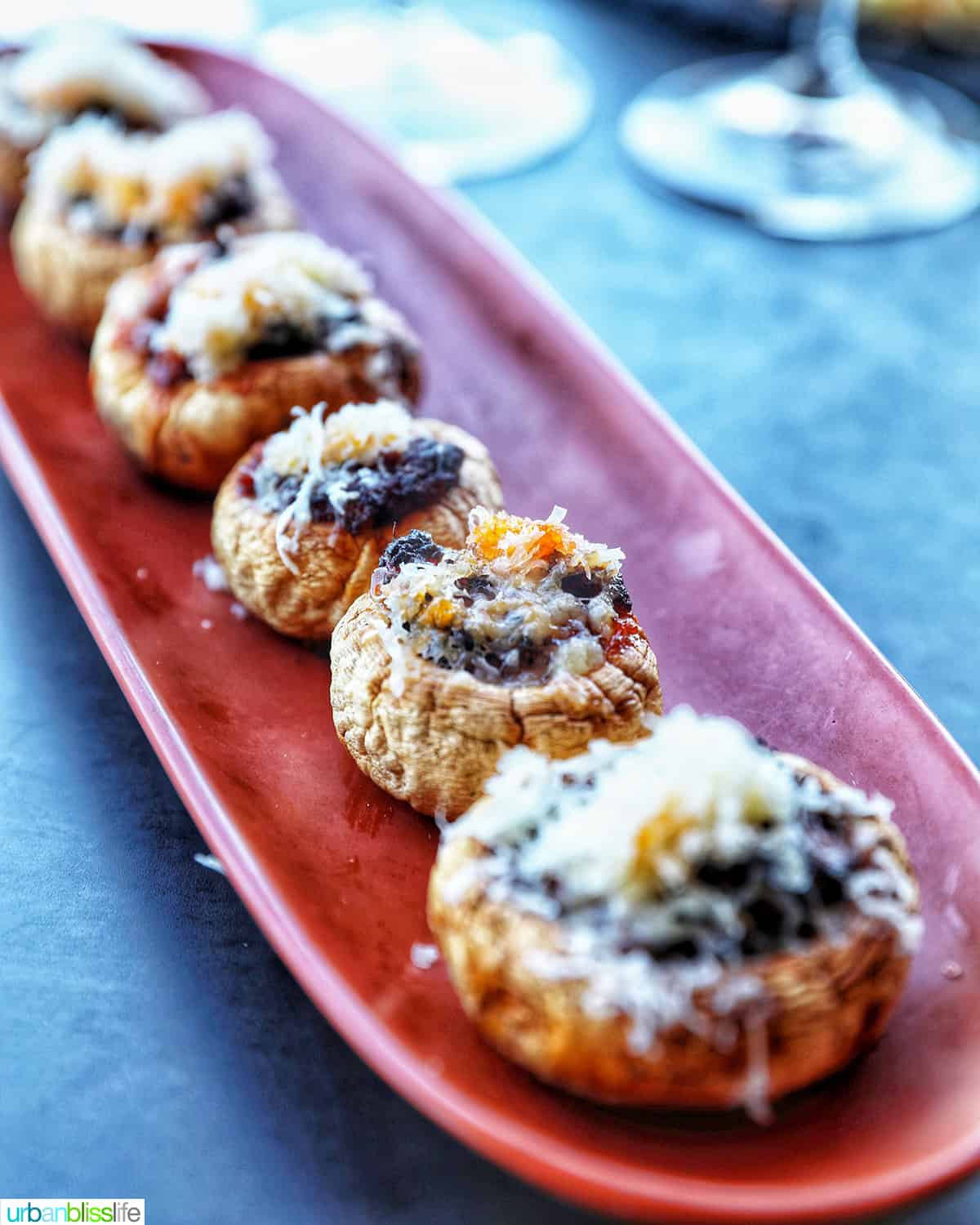 orange thin serving platter with chorizo stuffed mushrooms on top and glass of wine in the background.